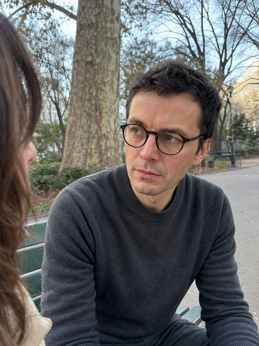 Mathis Laurent in a grey jumper, sitting on a park bench and listening to someone
